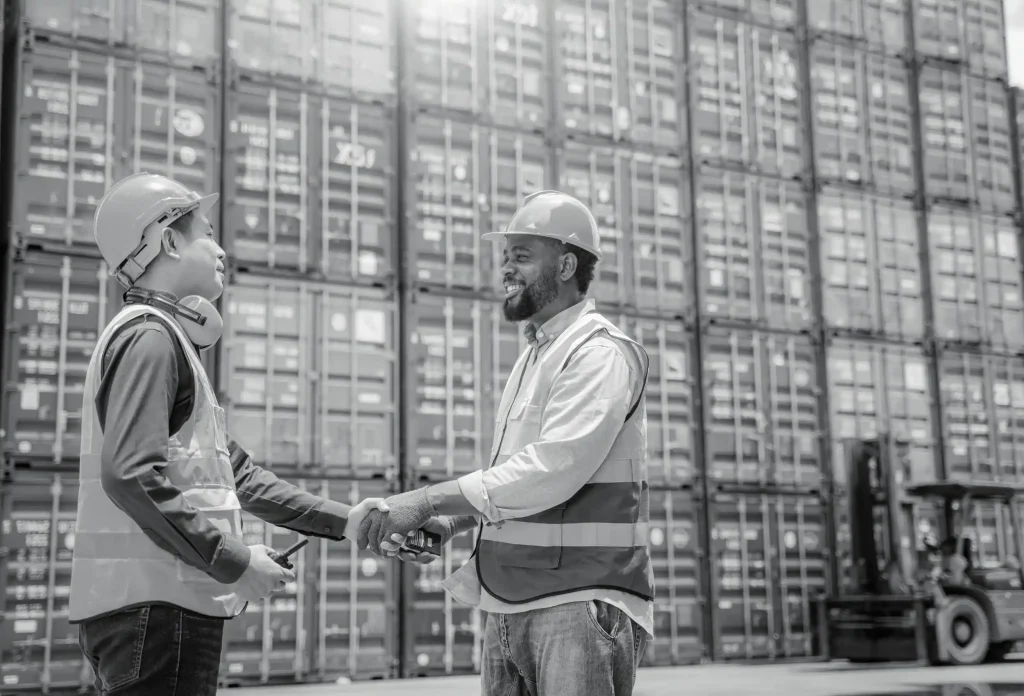 Warehouse worker in safety vest shaking hands with colleague near tall pallet racking