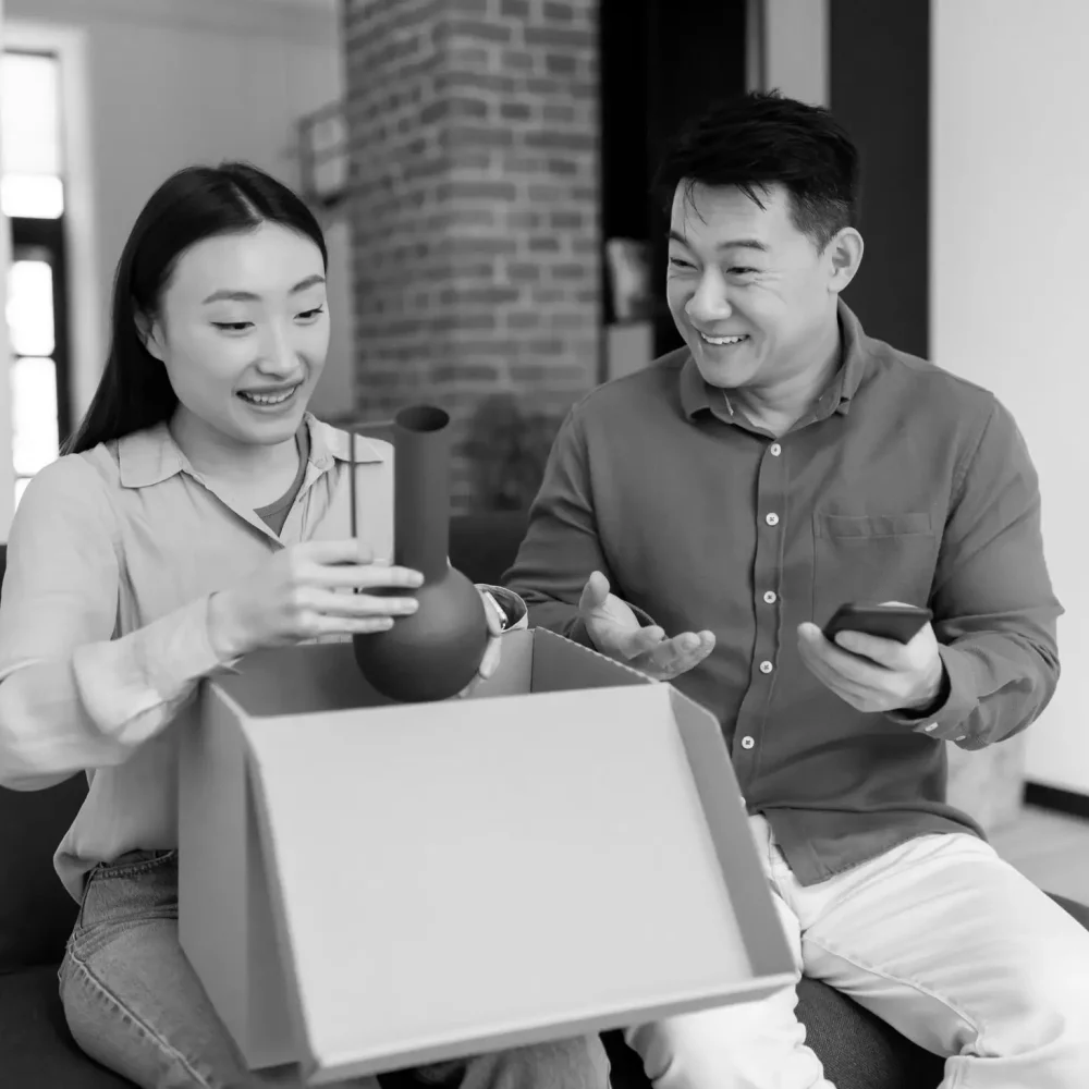 Smiling young couple happily packing items into cardboard box for shipment