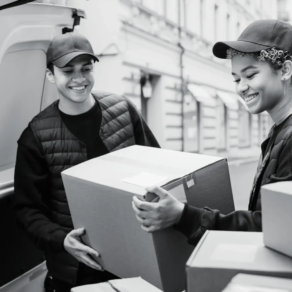 Smiling delivery couriers carrying cardboard boxes for customer shipment