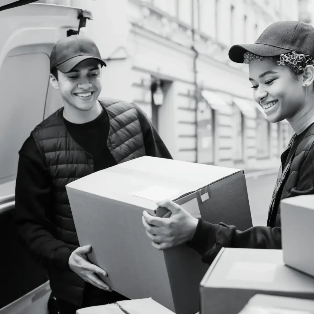 Male and female warehouse staff carrying large cardboard boxes together in fulfillment center